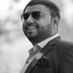 Stylish man in sunglasses and suit smiling outdoors in black and white