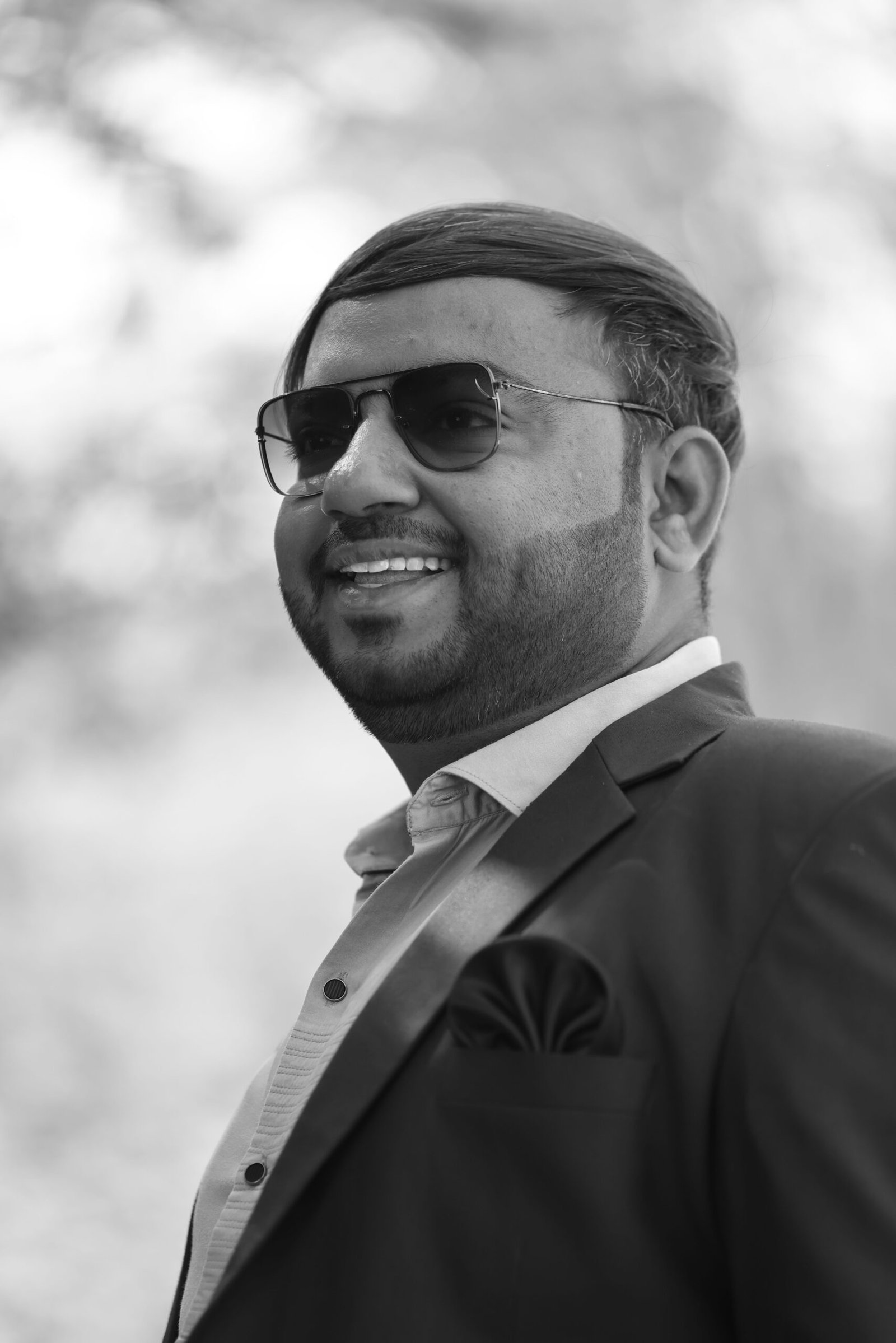 Stylish man in sunglasses and suit smiling outdoors in black and white