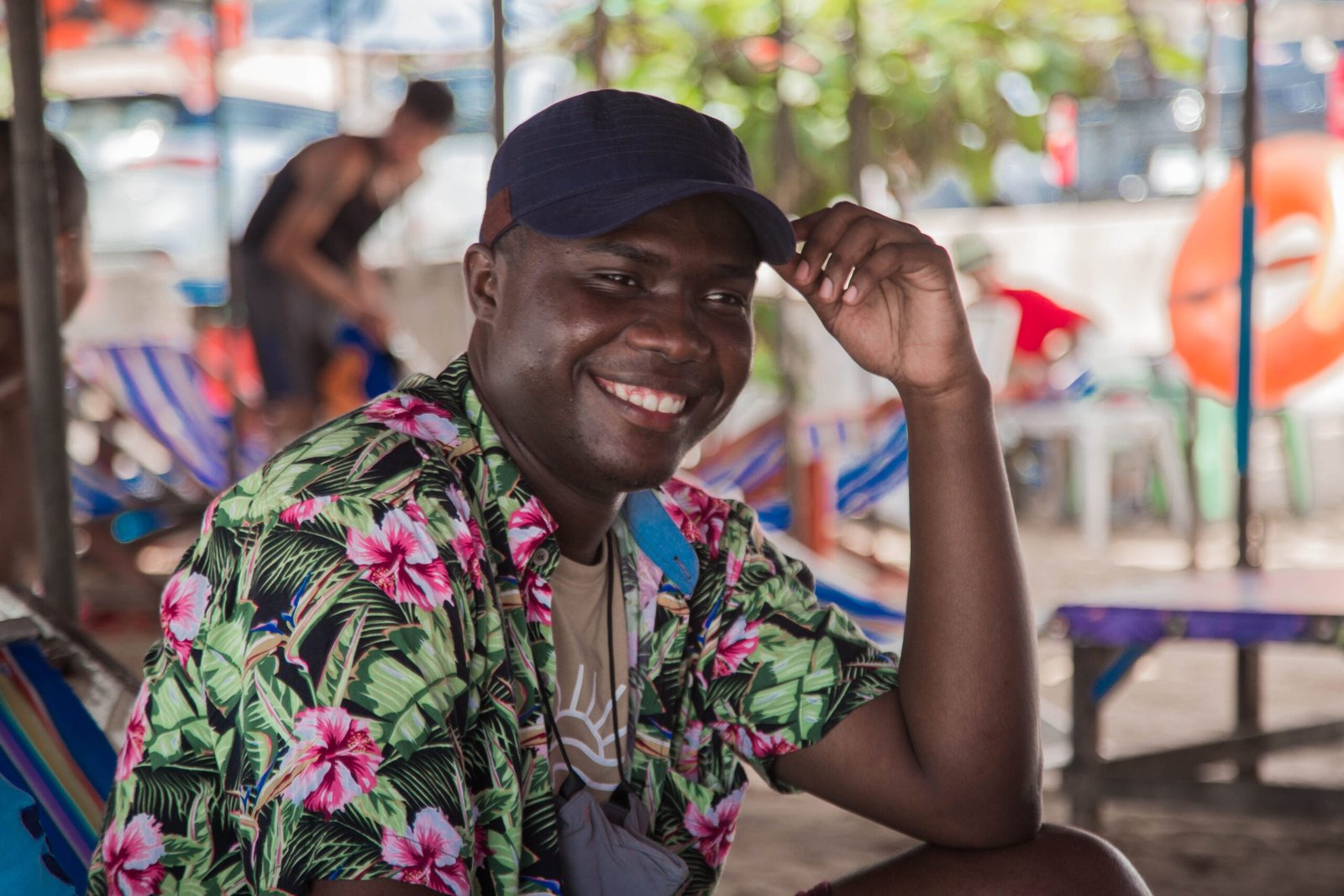 A cheerful man wearing a Hawaiian shirt relaxes at a vibrant beachside setting with lounge chairs.