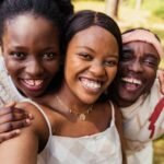 Three friends laughing and taking a selfie outdoors, showcasing happiness and friendship.
